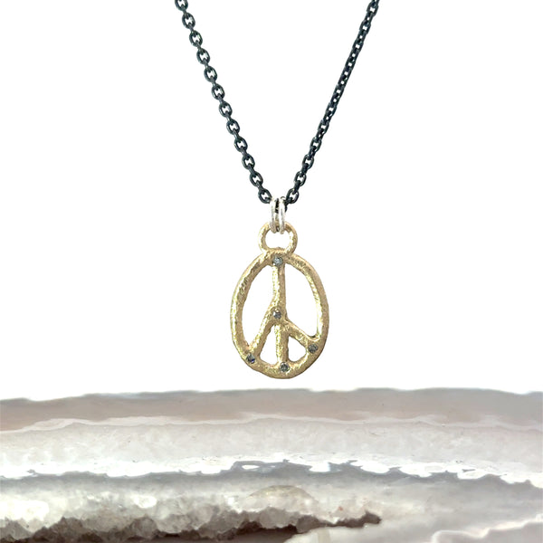 A gold peace sign pendant necklace with salt and pepper diamond accents on an oxidized sterling silver chain