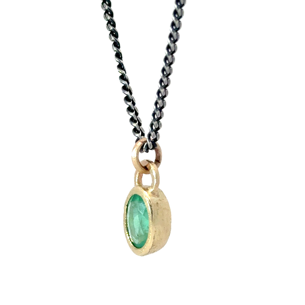 A gold pendant necklace featuring an oval-cut green gemstone in a textured bezel setting, suspended from a dark oxidized chain against a plain white background.