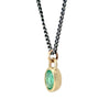 A gold pendant necklace featuring an oval-cut green gemstone in a textured bezel setting, suspended from a dark oxidized chain against a plain white background.